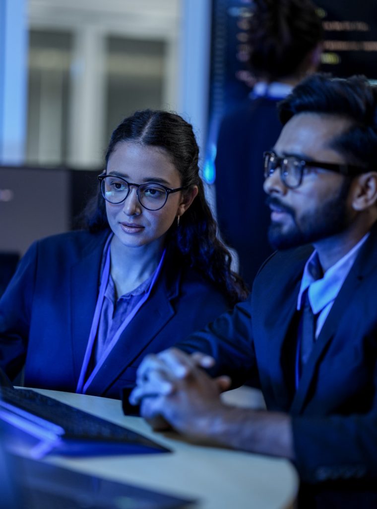 A diverse team of AI developers collaborates on a night coding session. A senior engineer oversees his team, intensely focused on debugging a complex machine learning project.