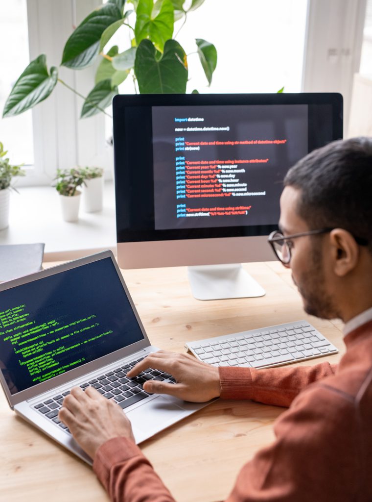 Over shoulder view of young web developer sitting at desk and working with laptop while creating computer algorithm