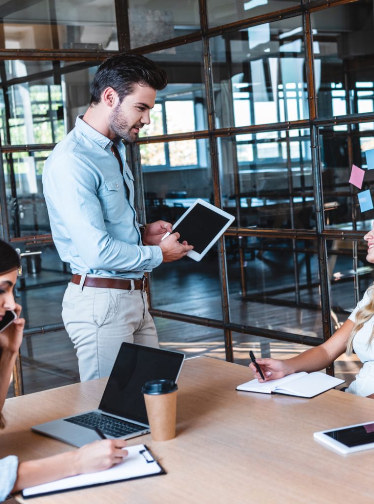 young businessman using digital tablet and looking at smiling female colleague at workplace